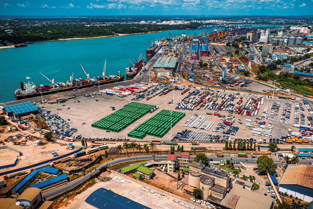View of the harbour in Dar es Salaam, Tanzania. On the left, a cargo ship in the harbour; on the right, storage areas with containers and vehicles.