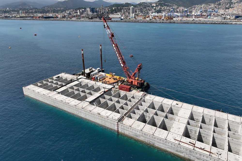 View of the port of Genoa; in the foreground, a crane on a concrete structure in the sea