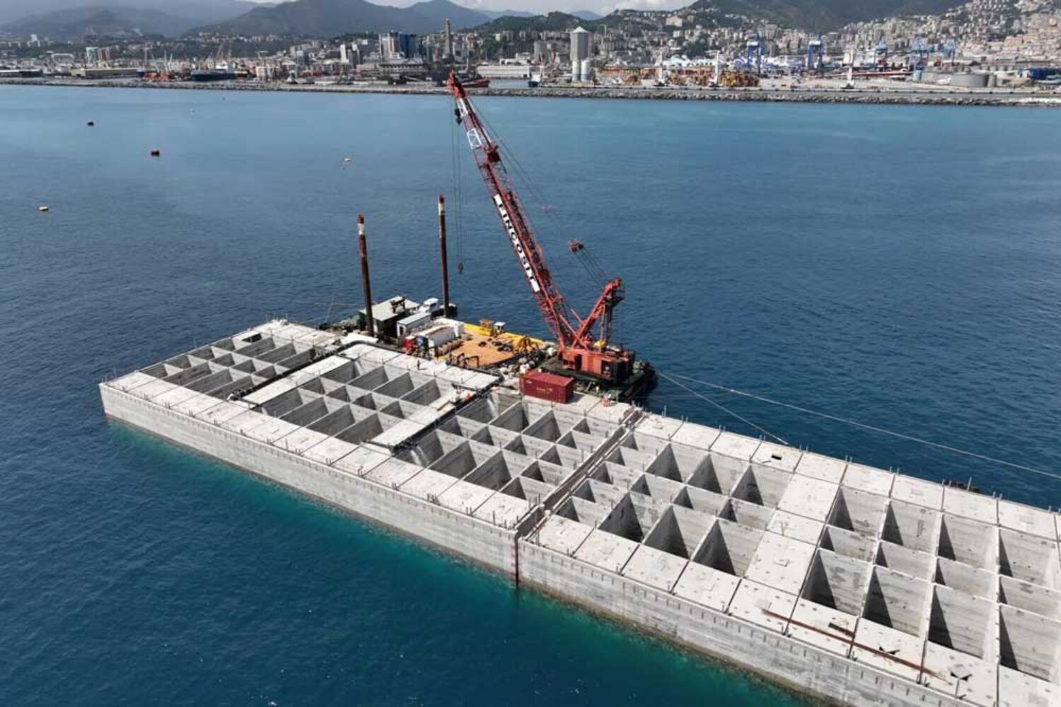 View of the port of Genoa; in the foreground, a crane on a concrete structure in the sea