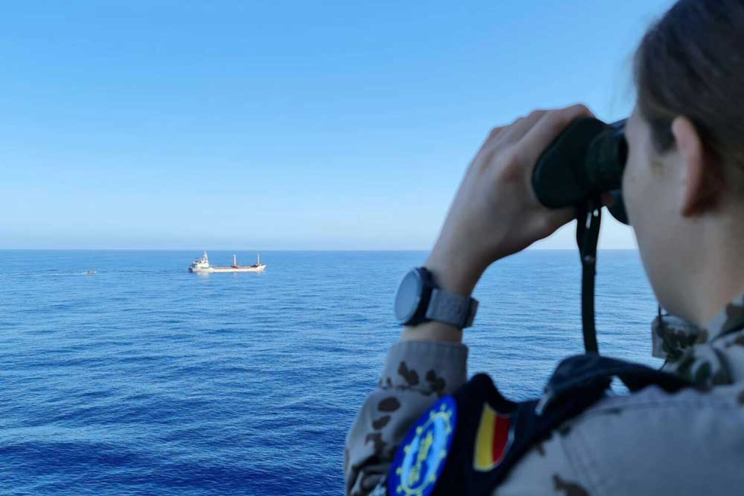 A person is watching a cargo ship in the Mediterranean